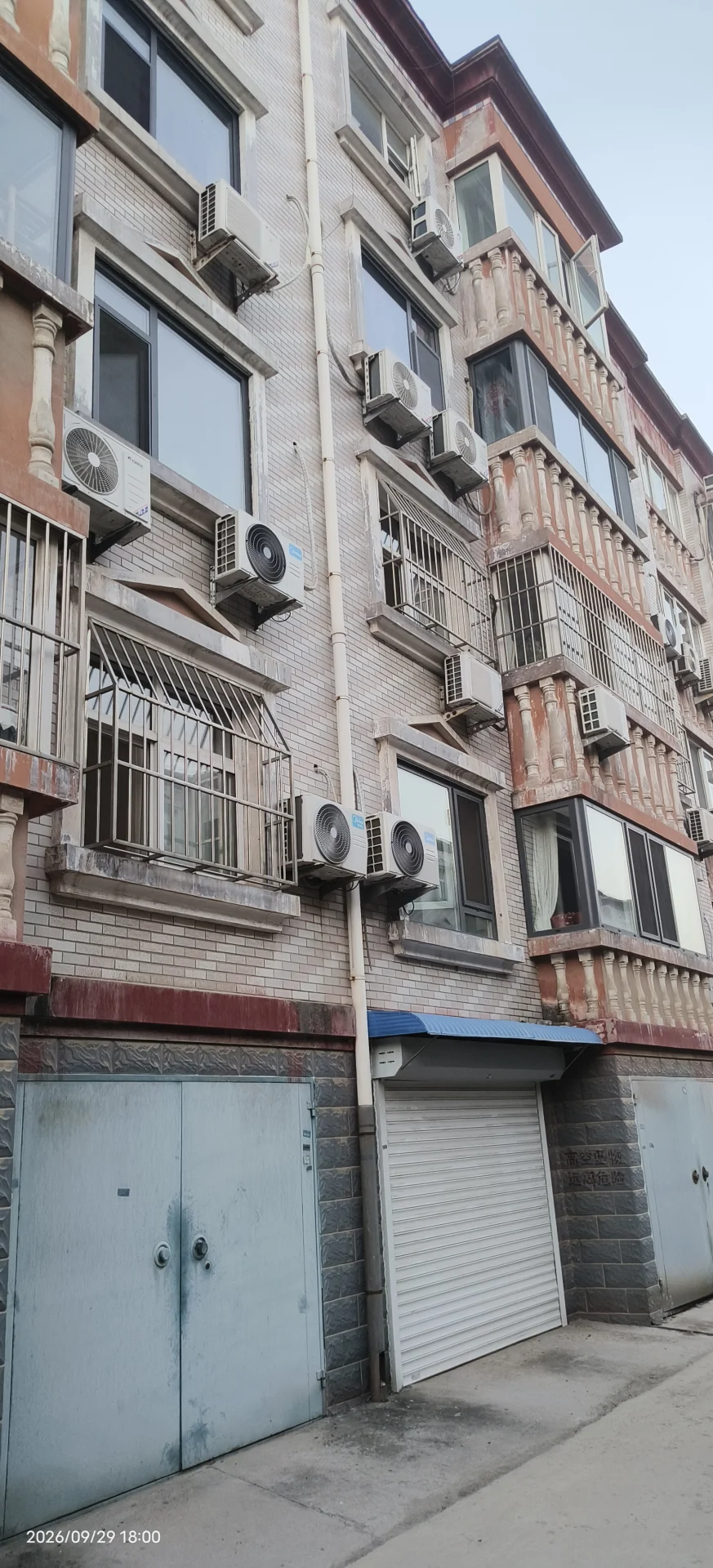 一栋多层住宅建筑，外墙呈浅色砖砌结构，配有多个空调外机安装在窗边。建筑风格偏向实用型，整体环境为城市街道景观。