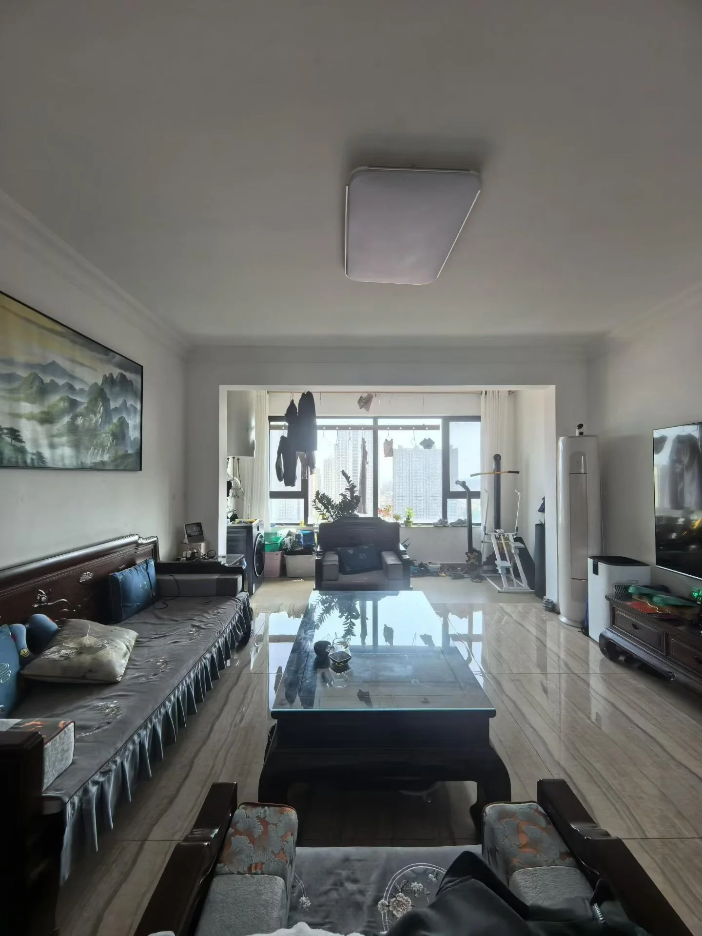 客厅空间，地面采用浅色木纹瓷砖，配有深色沙发和玻璃茶几。房间采光适中，整体装修风格偏向传统或实用的居住环境。