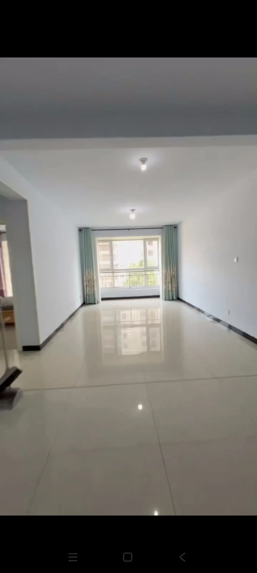 一个宽敞的室内空间，地面铺设光洁的大面积瓷砖，墙面为白色，采光良好。整体装修风格简洁明亮，呈现出基础且现代的居住环境。
