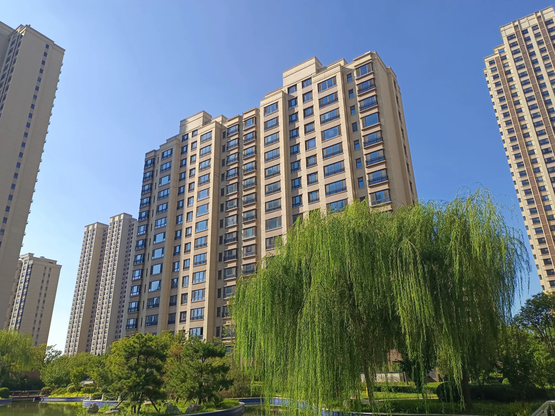 一座大型现代风格的住宅建筑，周围环绕着茂密的绿植和水景，天空晴朗，整体环境宁静宜人。