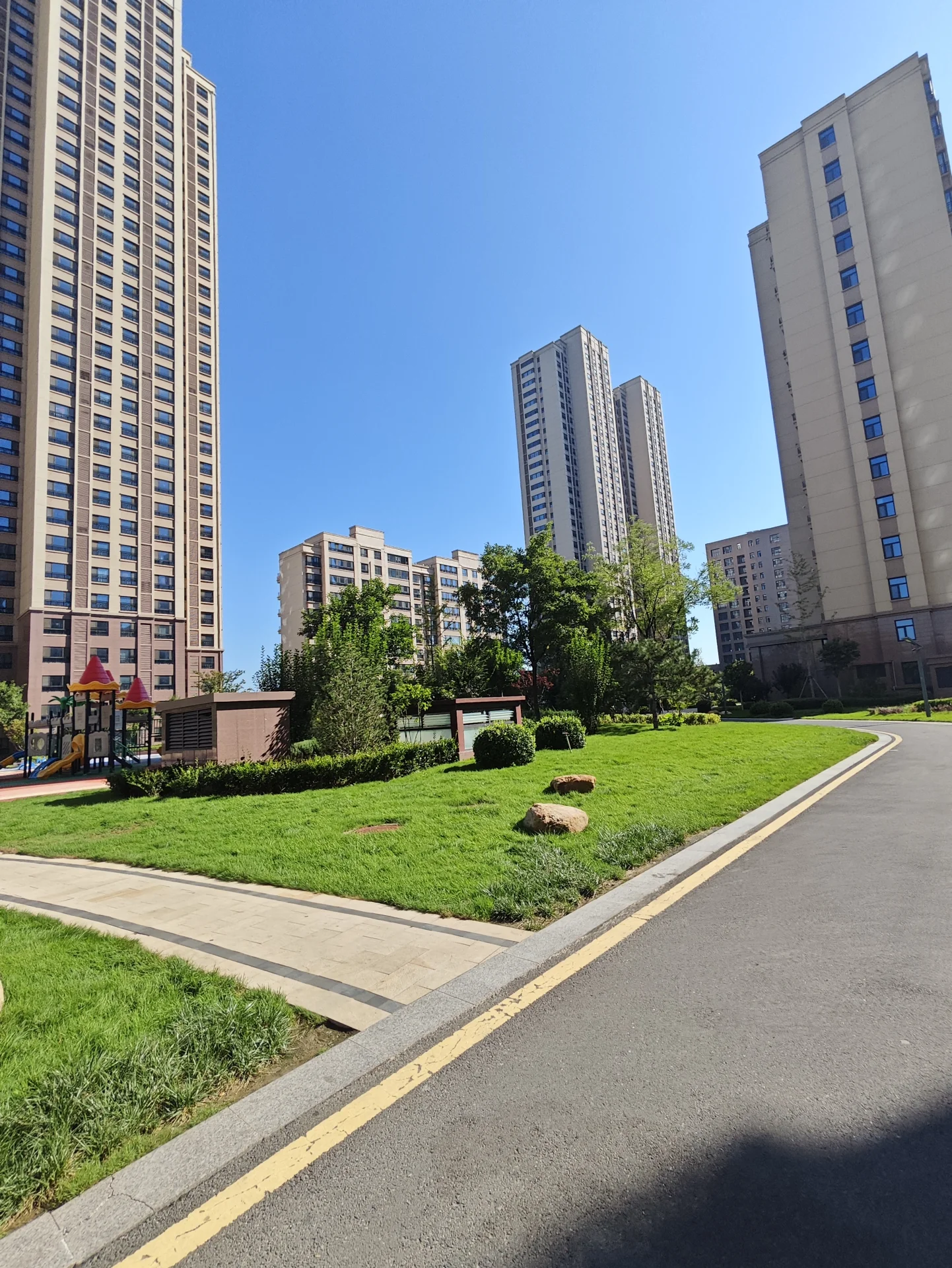 多栋高层住宅建筑环绕在开阔的绿化区域，道路平整，绿植修剪整齐。整体环境展现出现代城市居住区宁静和谐的氛围。