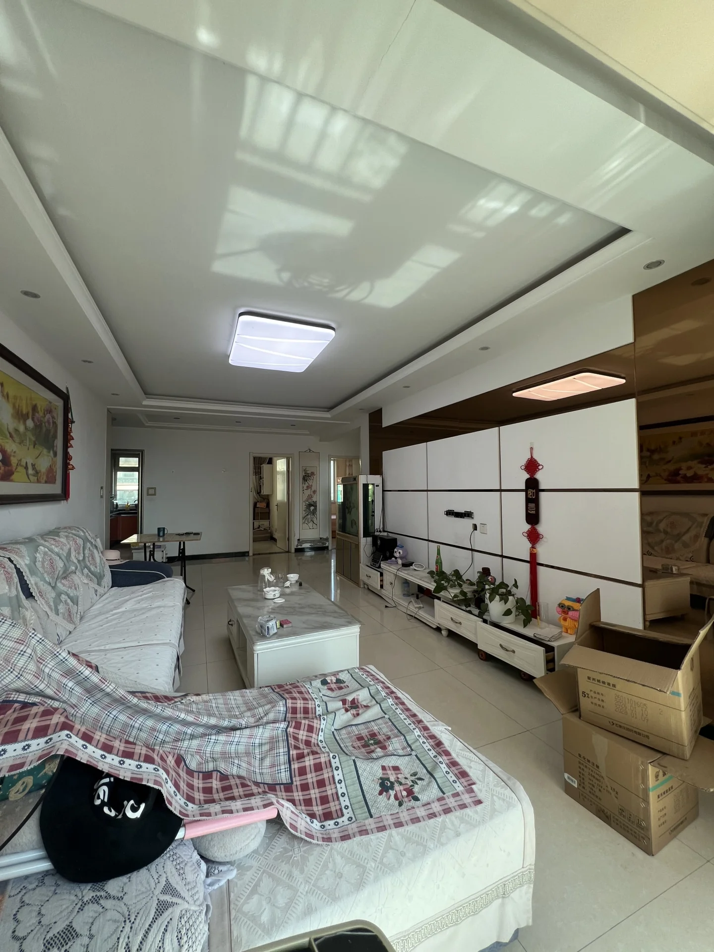 这是一个空置的室内空间，地面铺设浅色瓷砖，天花板采用白色吊顶设计。房间内摆放着几张床和一些家具，整体装修风格偏基础实用，采光良好。