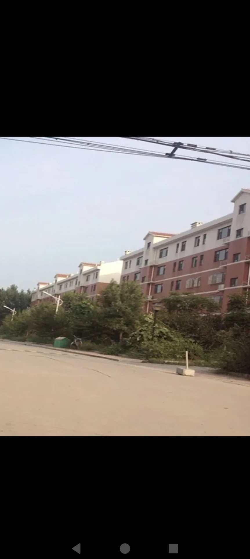 一座多层现代风格的住宅建筑，外立面采用红白相间的色调，周围有植被环绕，整体环境开阔。