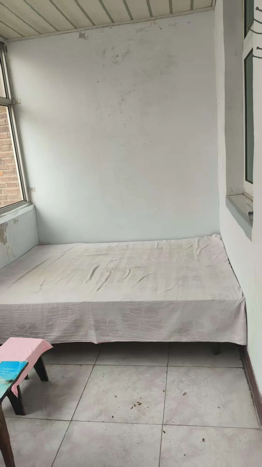 卧室空间，墙面和地面基础装修，配有床和小型床头柜。采光适中，整体呈现基础、未精细化的居住环境。
