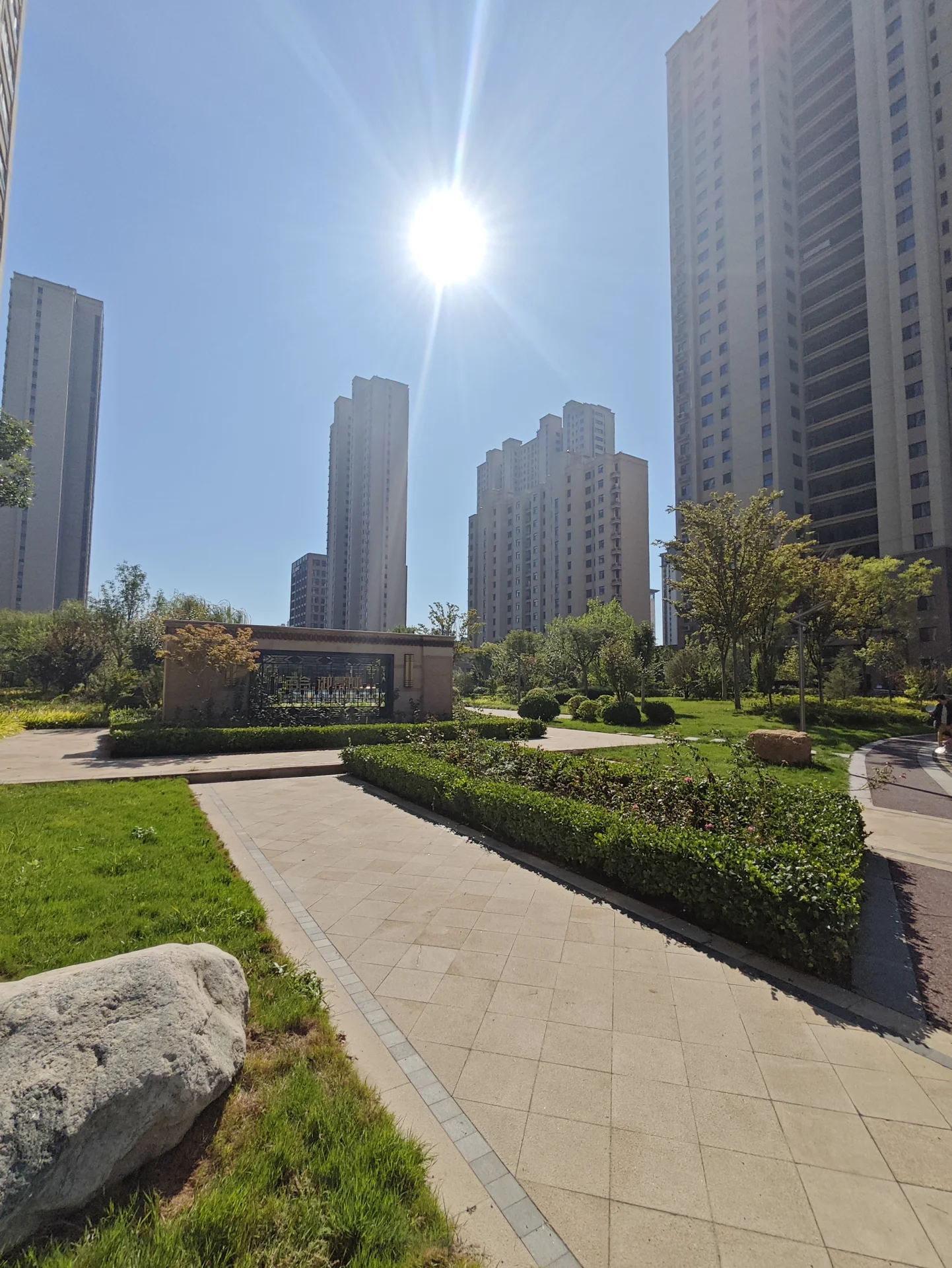 现代高层住宅群的外部景观，建筑立面简洁，周围绿化覆盖良好，阳光明媚，整体呈现现代都市居住环境的开阔感。