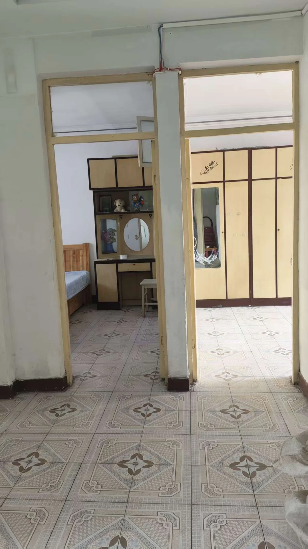 这是一个室内空间，地面铺设着带有几何图案的瓷砖，房间内可见床、梳妆台等基础家具，整体环境较为基础，光线均匀。