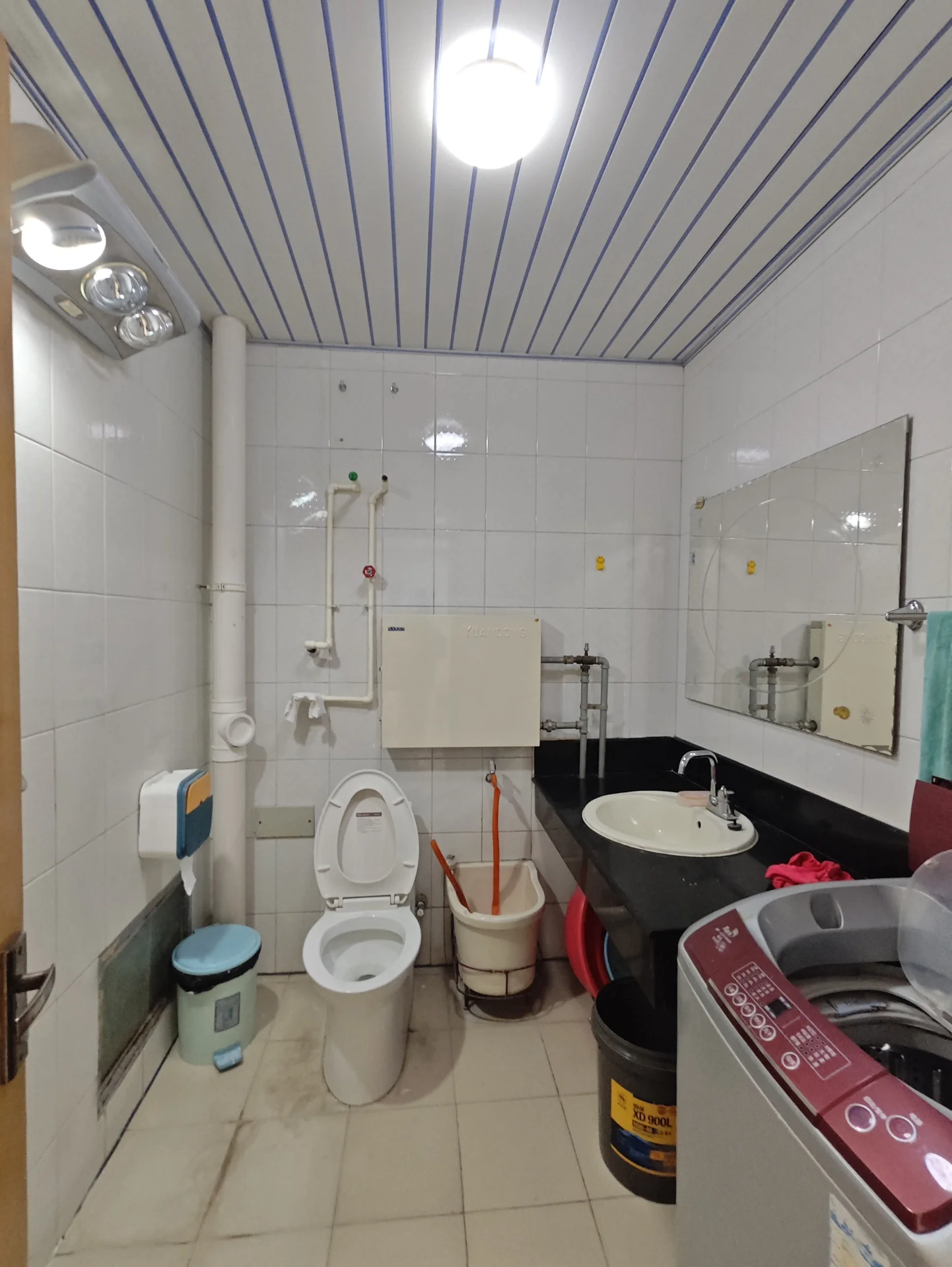 卫生间空间，墙面和地面铺设白色瓷砖，配有白色马桶、洗手台及淋浴区域。天花板采用蓝色线条装饰，整体光线明亮，具备基础的卫浴设施。