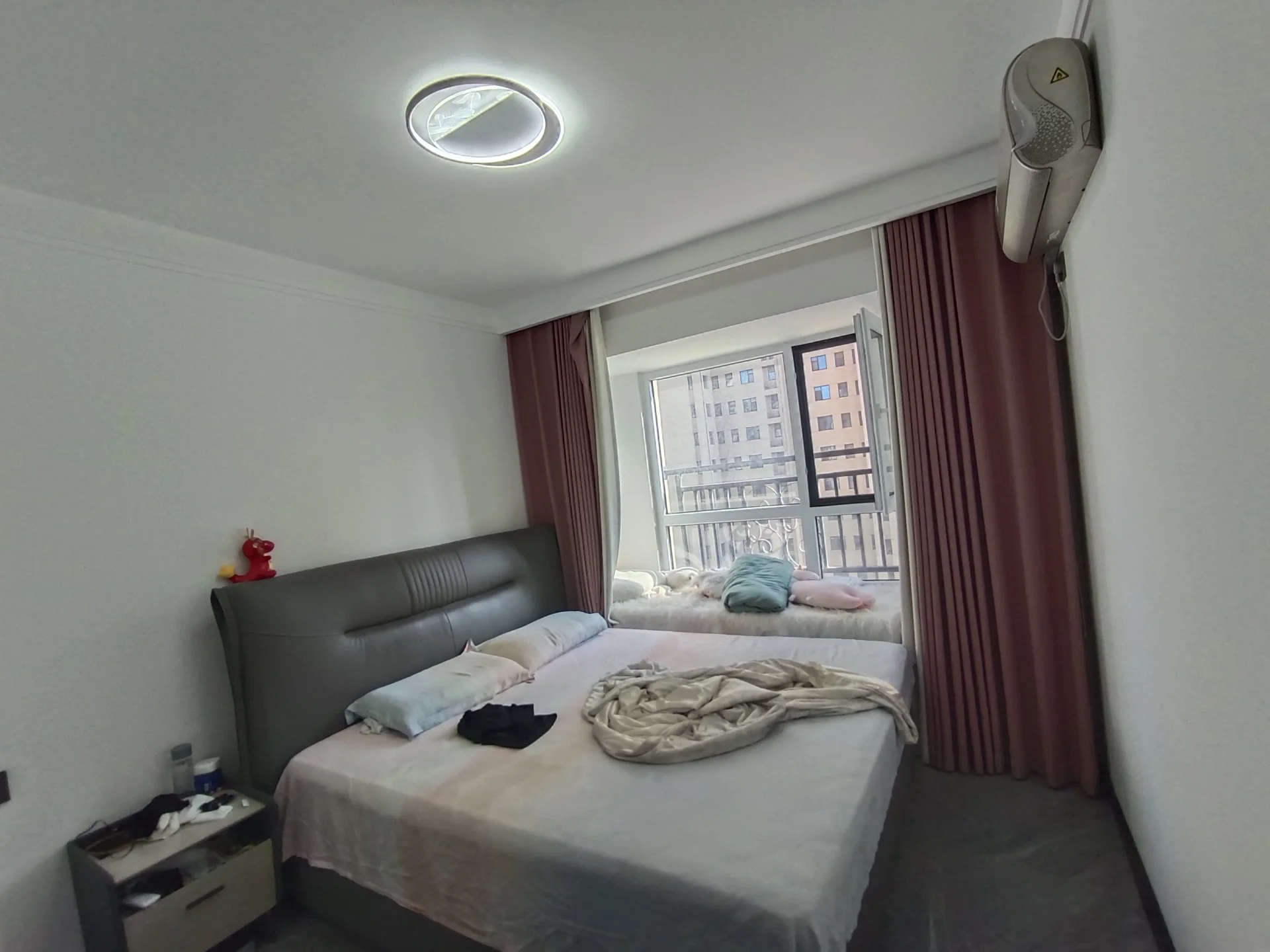 卧室空间，床铺为深色软包材质，搭配白色床品和灰色被子。房间内光线适中，整体装修风格偏向现代简约，环境整洁。