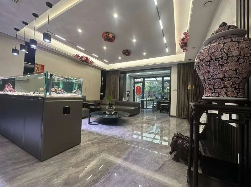 这是一个宽敞的室内展示空间，地面铺设大理石纹瓷砖，天花板设计现代简洁。空间内陈列着一个大型的展示柜，并配有沙发和茶几作为休息区。整体采光良好，装修风格偏向现代商业或高端会客环境。