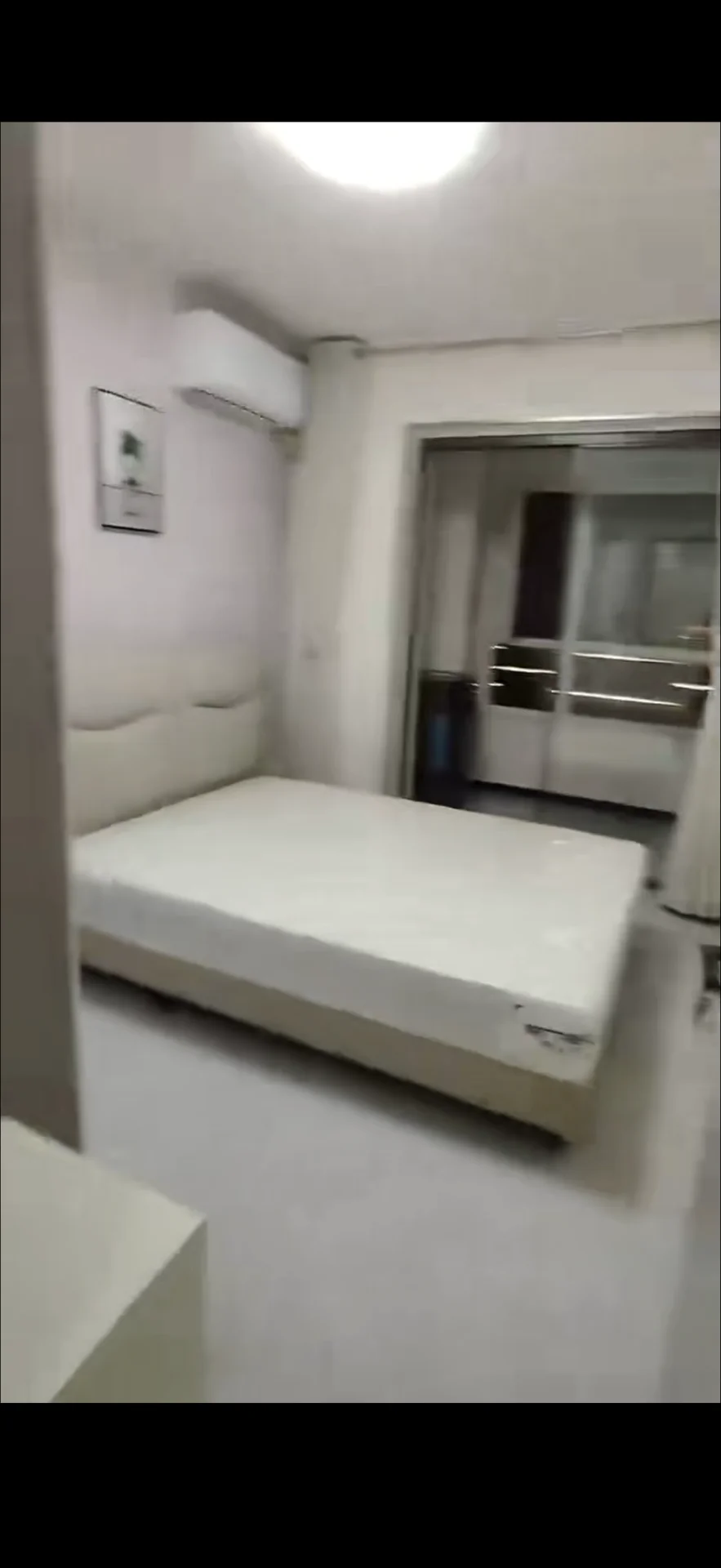 卧室空间，墙面和地面采用浅色调，配有大型床铺和空调设备。采光适中，整体呈现简洁明亮的现代风格。