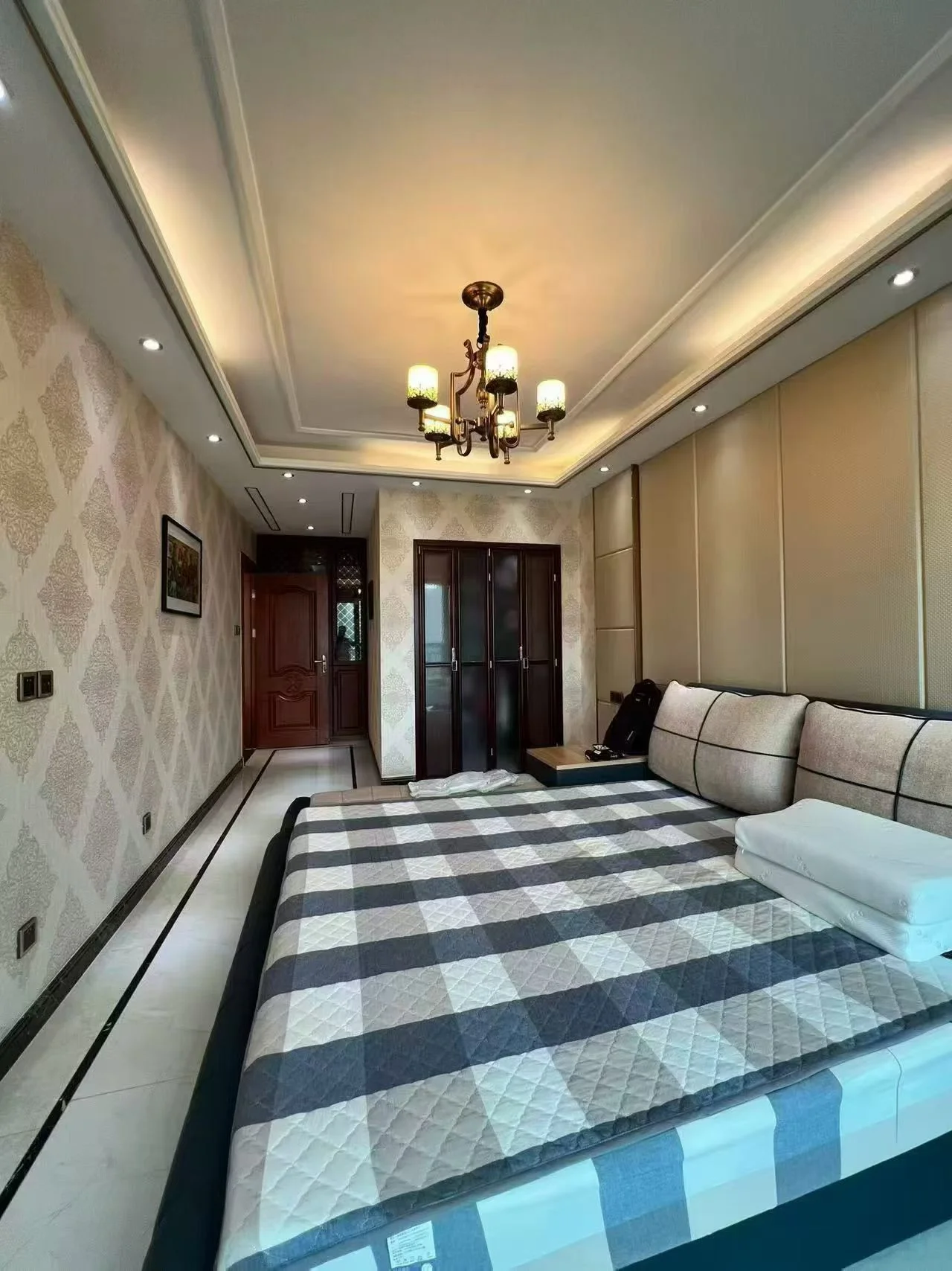 卧室空间，床铺采用黑白格纹床品，配有简约的沙发和吊灯照明。房间内装修风格偏向现代简约，采光适中，整体环境整洁舒适。