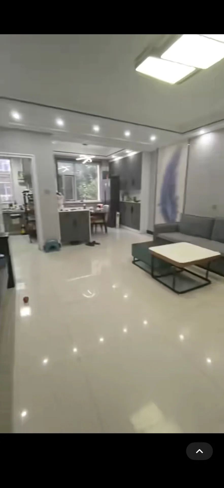 这是一个开放式起居空间，地面铺设大尺寸白色瓷砖，整体装修风格偏现代简约。空间布局宽敞，采光良好，家具配置以沙发和茶几为主。
