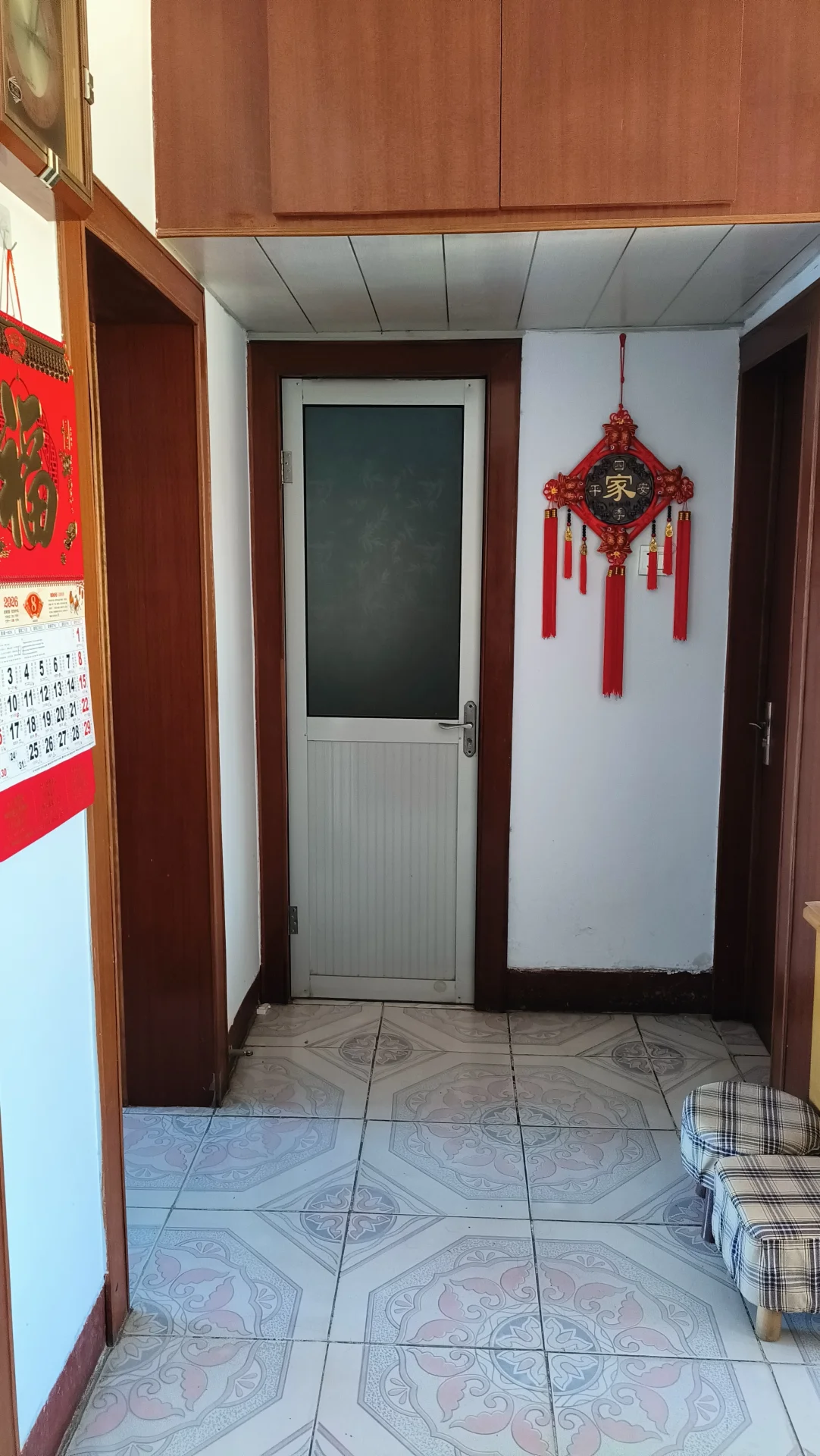 这是一个住宅的入口区域，地面铺设着带有复杂花纹的瓷砖，墙面简洁，门口悬挂有红色装饰灯笼。整体环境整洁，具有典型的居住氛围。