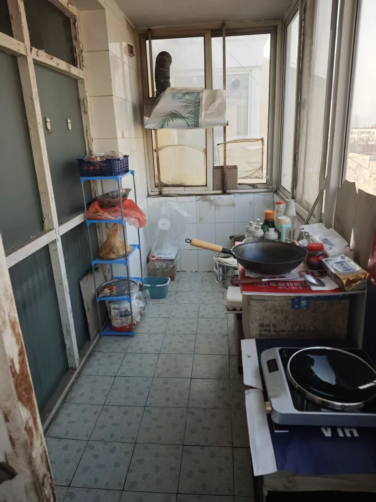 一个开放式的室内空间，地面铺设浅色瓷砖，墙面为白色或浅色调。空间内摆放着储物架、厨具和一些生活用品，整体环境较为简朴实用。