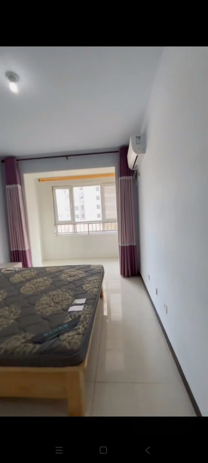 卧室空间，地面铺设浅色瓷砖，配有大型床铺和窗户。房间采光良好，整体装修风格简洁明亮，具备基础的居住功能。
