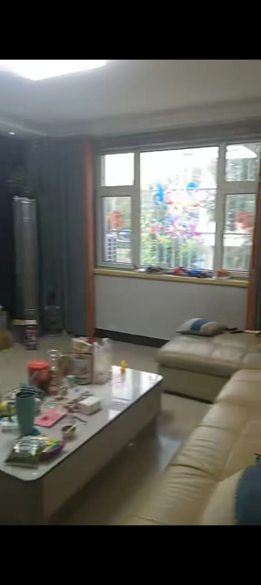 客厅场景，家具以米色沙发为主，配有长条式茶几和大型冰箱等家电。空间采光良好，整体呈现基础的现代装修风格，氛围整洁。