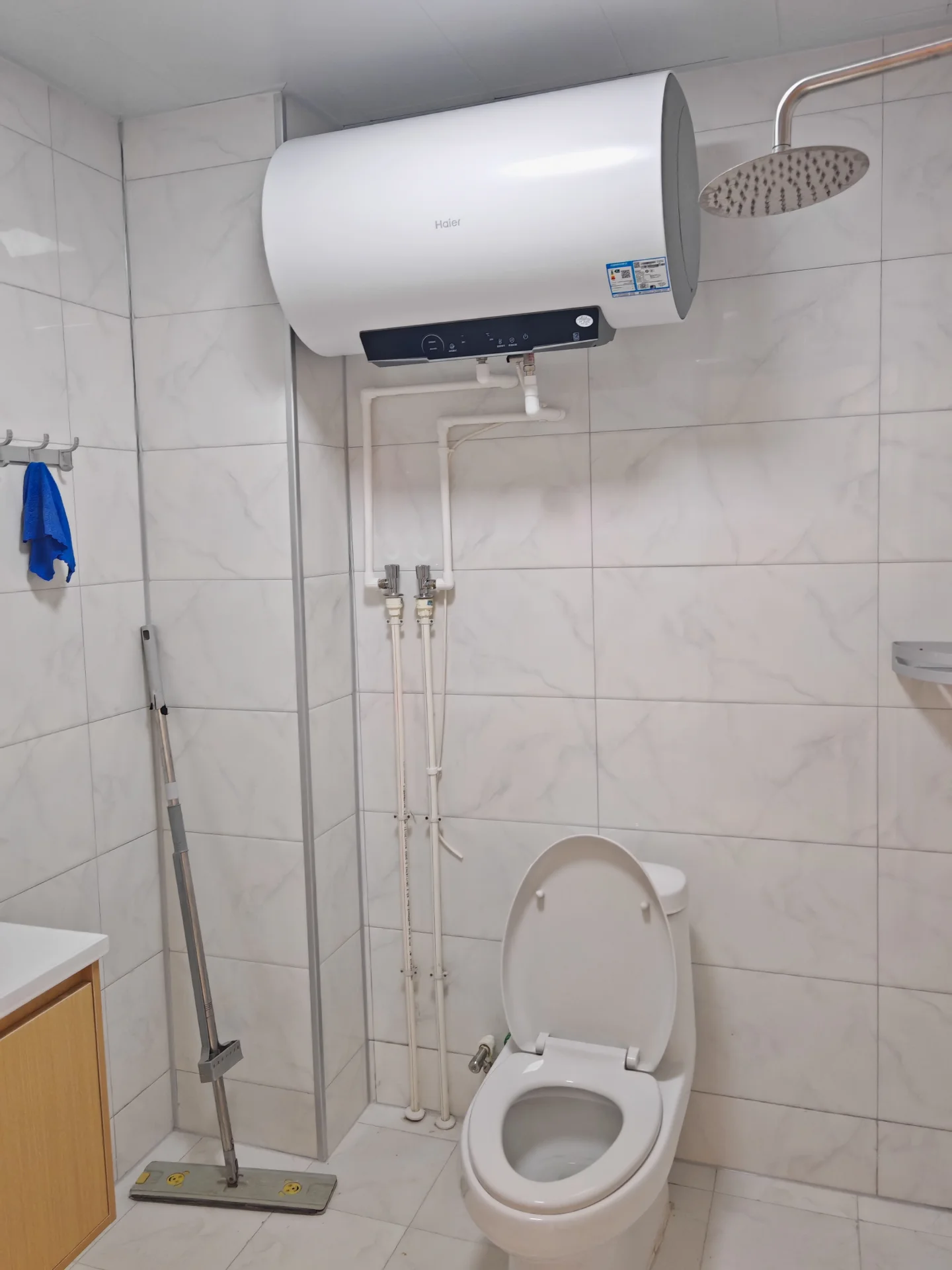 卫生间空间，墙面和地面铺设白色大尺寸瓷砖，安装有大型白色恒温花洒和马桶。整体装修风格简洁明亮，采光良好，具备基础的卫浴功能。