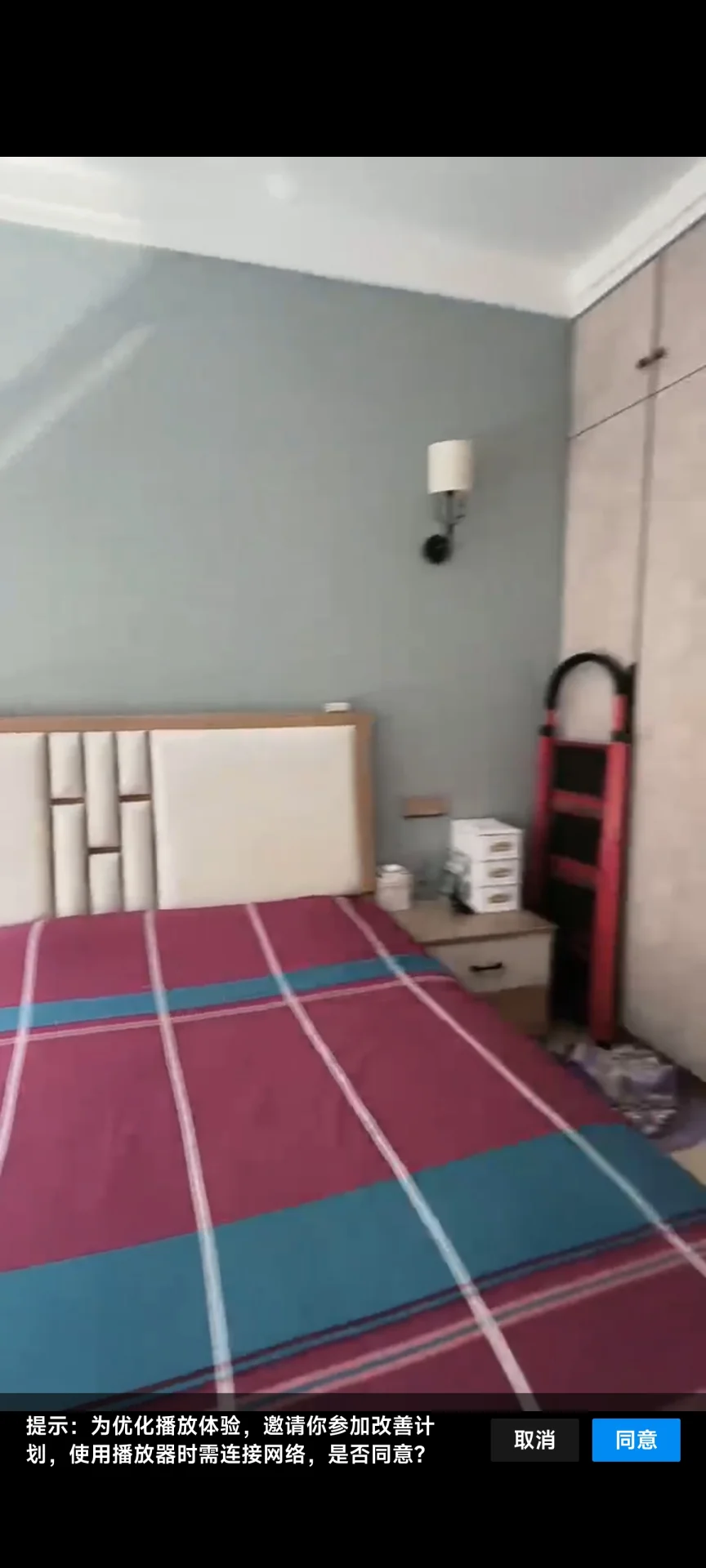 卧室空间，床铺占据主体，床头板为白色木质设计。墙面呈浅灰色调，配有壁灯照明。整体环境简洁，光线适中。