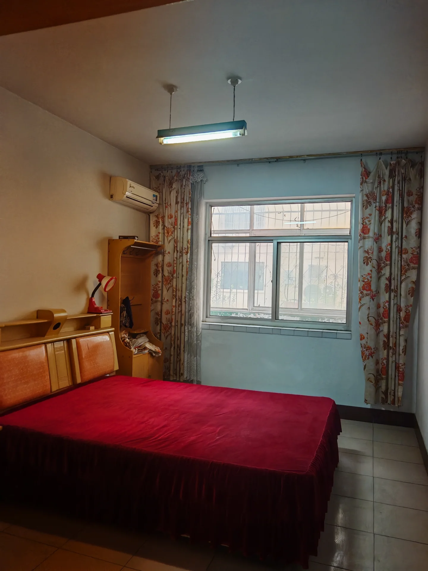 卧室空间，床铺采用红色大件家具，配有简约的衣柜和空调设备。房间采光适中，整体呈现基础的居住环境。