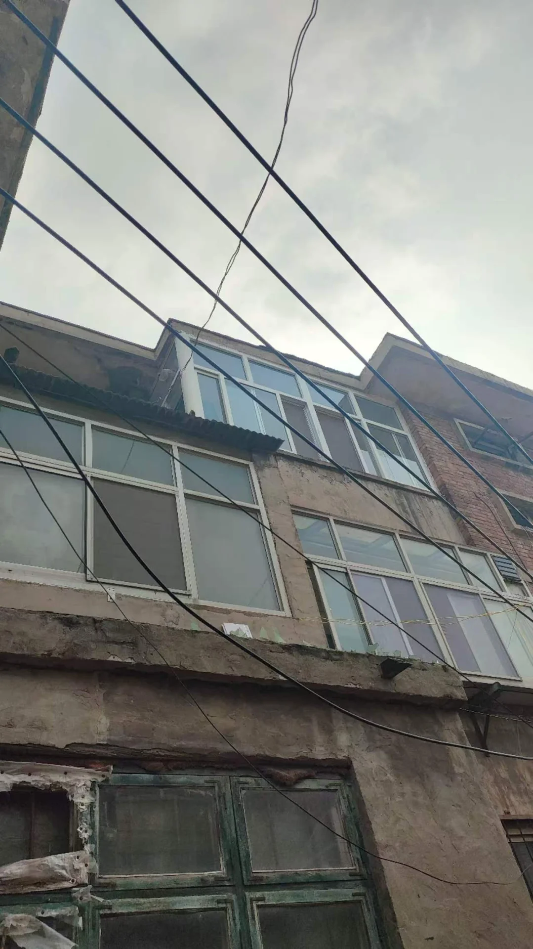 一栋多层建筑的立面，外墙呈浅色调，窗户分布均匀，上方有密集的电线穿过画面。整体风格较为朴素，展现出城市居住环境的特征。