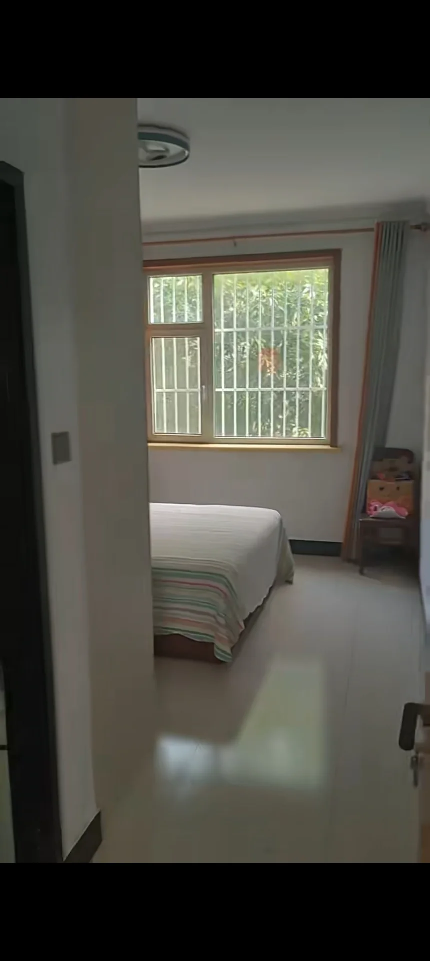卧室空间，墙面和地面采用浅色调，配有单张床铺和衣柜。采光良好，整体呈现简洁明亮的现代风格。