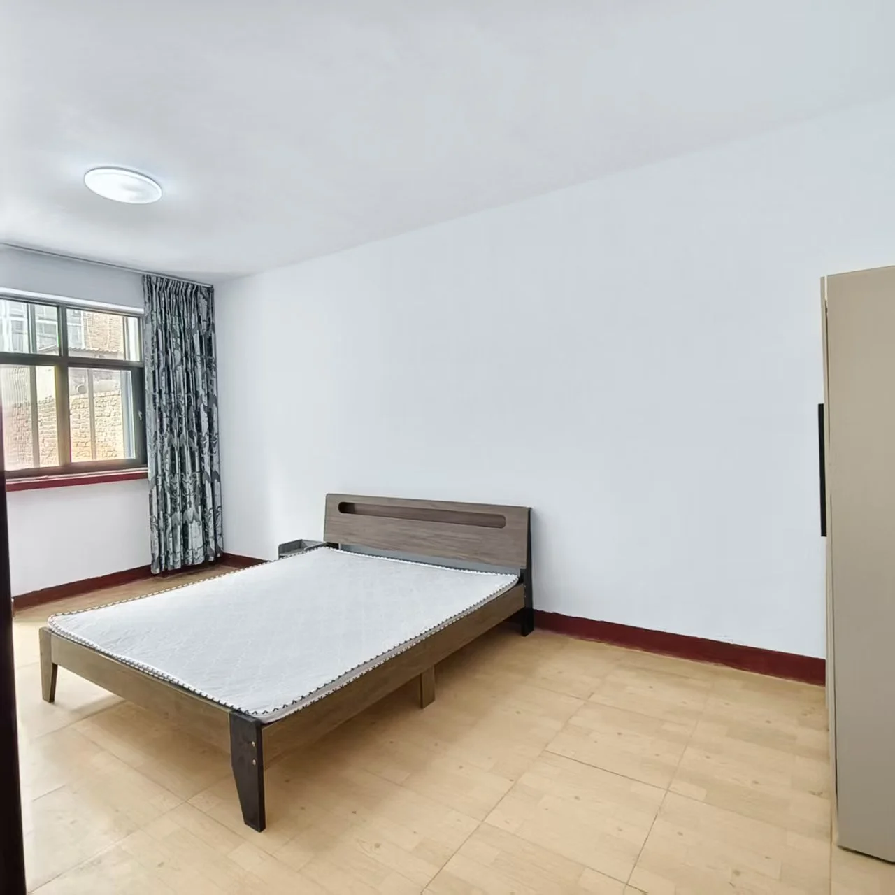 卧室空间，床铺为深色木质框架，搭配白色床品。房间内采光良好，墙面简洁，整体呈现基础的现代简约风格。