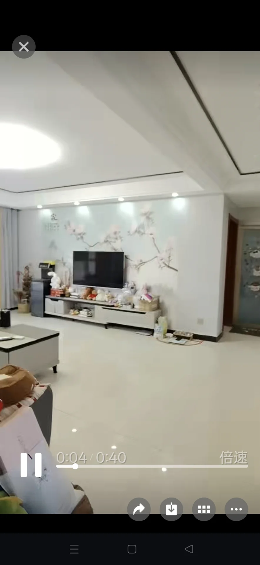 这是一个空旷的室内空间，地面为浅色瓷砖，墙面装饰有淡雅的花卉图案。房间内摆放着电视柜和部分家具，整体装修风格偏向现代简约，采光良好。