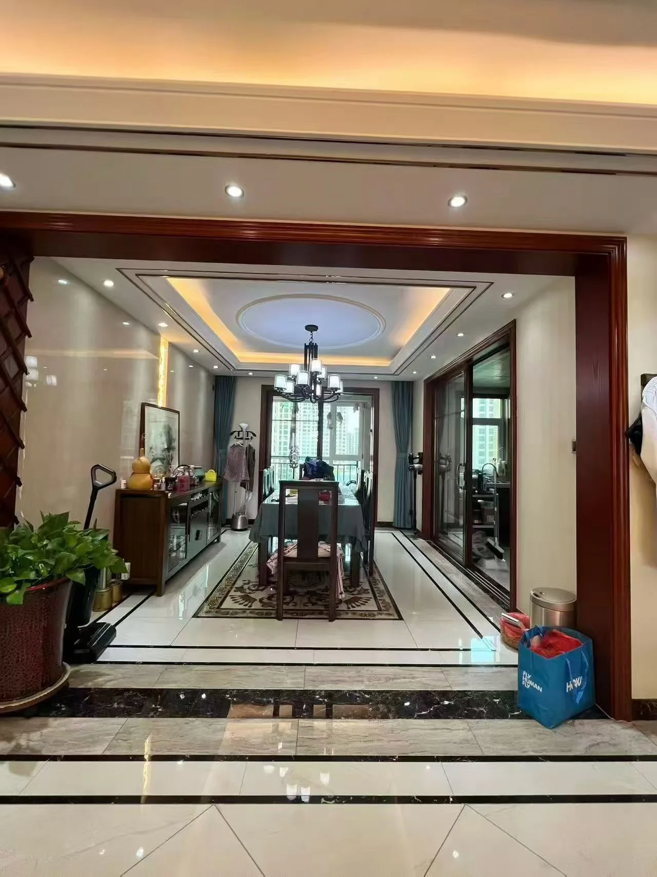 这是一个宽敞的室内空间，地面铺设大理石材质，中央摆放着餐桌和吊灯。空间采光良好，整体装修风格偏向现代简约，环境整洁。