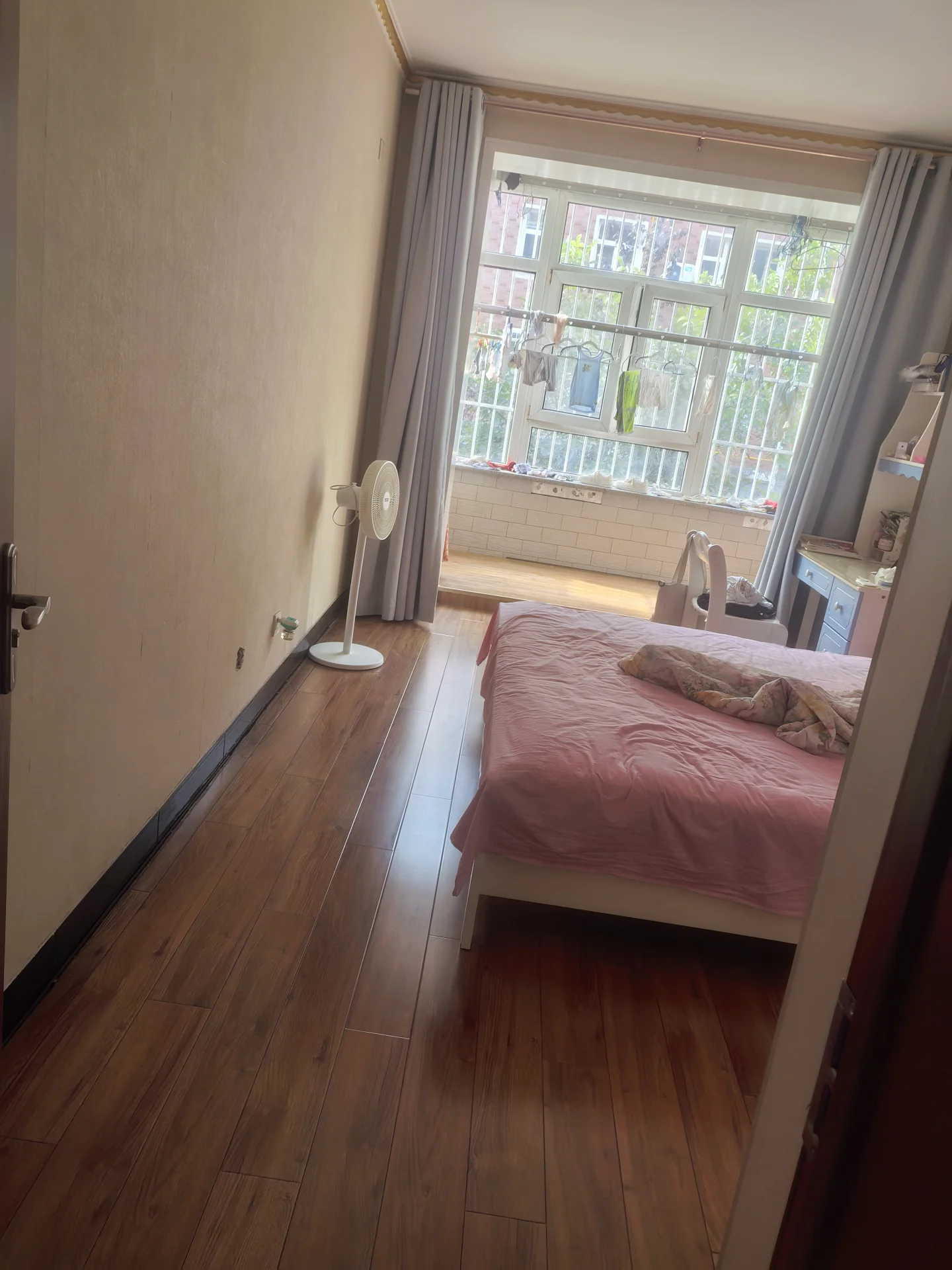 卧室空间，地面铺设木纹地板，配有粉色床品和落地灯。房间采光良好，整体呈现简洁舒适的居住氛围。