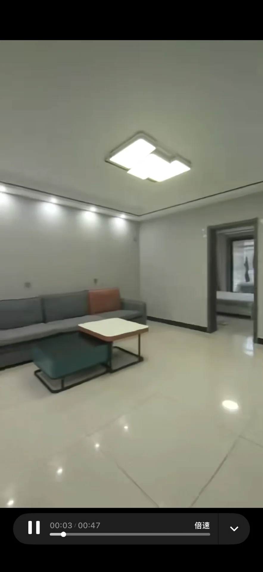 客厅空间，地面铺设浅色瓷砖，配有深色沙发和茶几。室内采光均匀，整体呈现现代简约风格，环境整洁明亮。