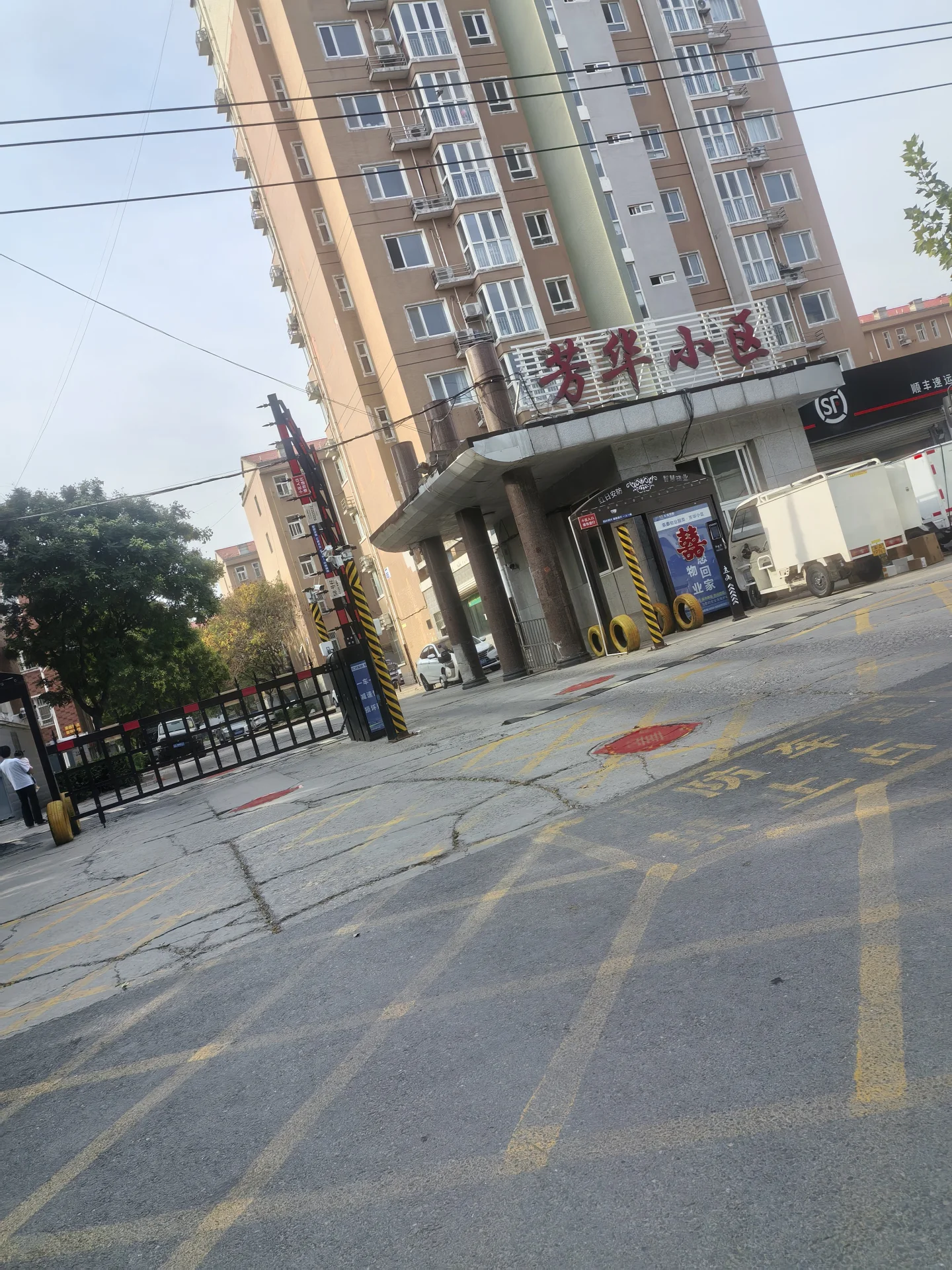 一栋多层住宅建筑立面，建筑风格偏现代，主体呈浅色调。建筑前方有道路和一些临时施工或活动设置，整体环境属于城市居住区。