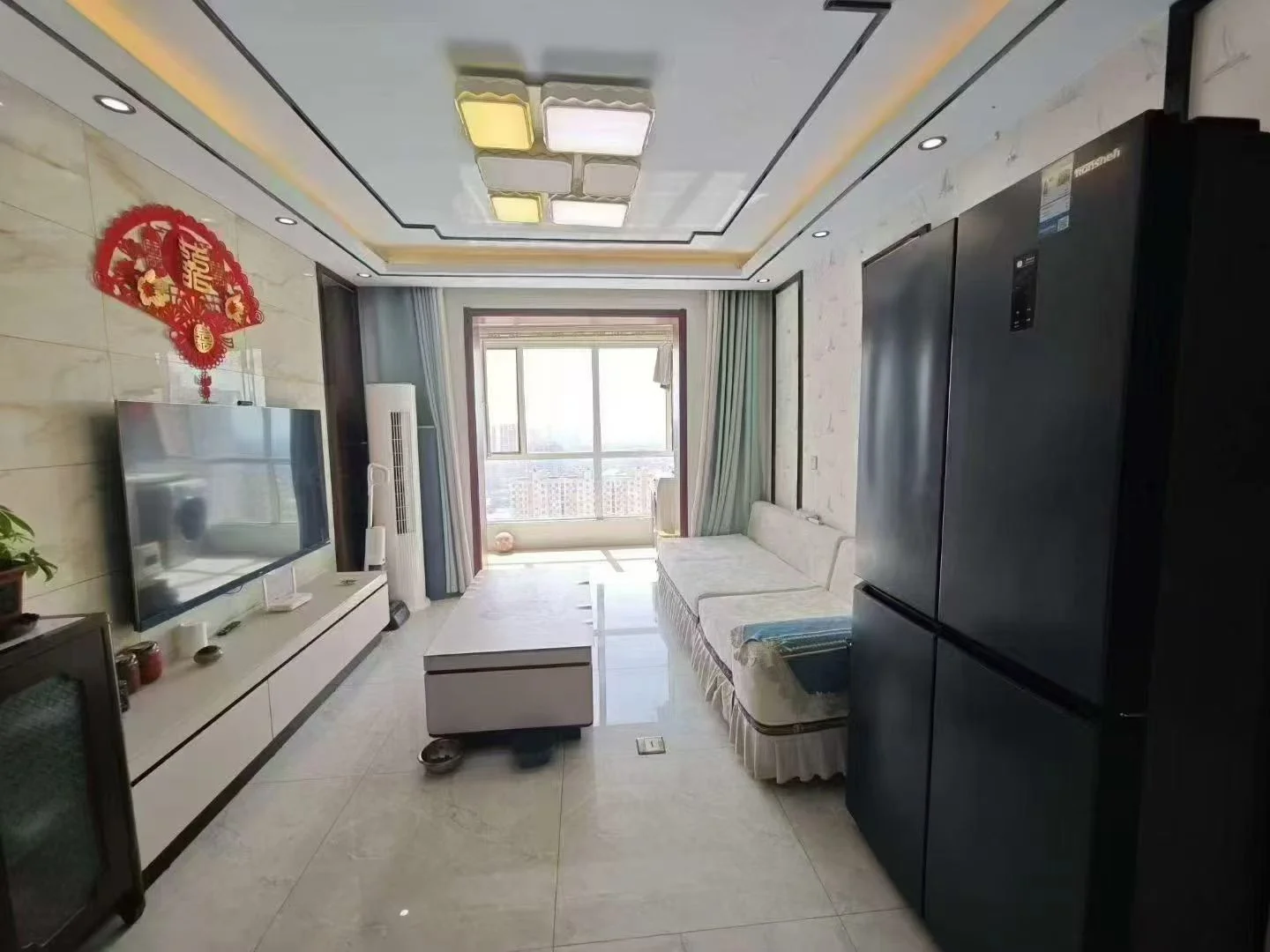 客厅空间，墙面和地面采用浅色大理石纹饰，配有大型电视墙和简约沙发。天花板设计有嵌入式灯带，采光良好，整体呈现现代简约风格。