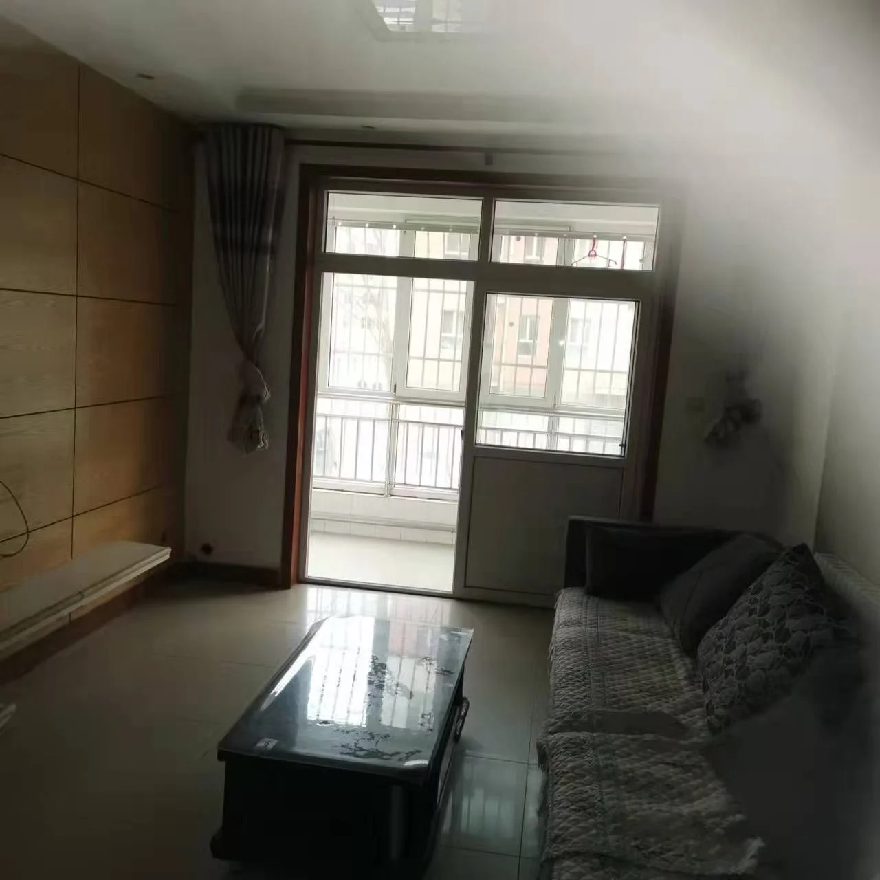 客厅空间，墙面采用米色调，配有深色茶几和布艺沙发。采光良好，整体呈现基础的居住环境，氛围较为朴素。
