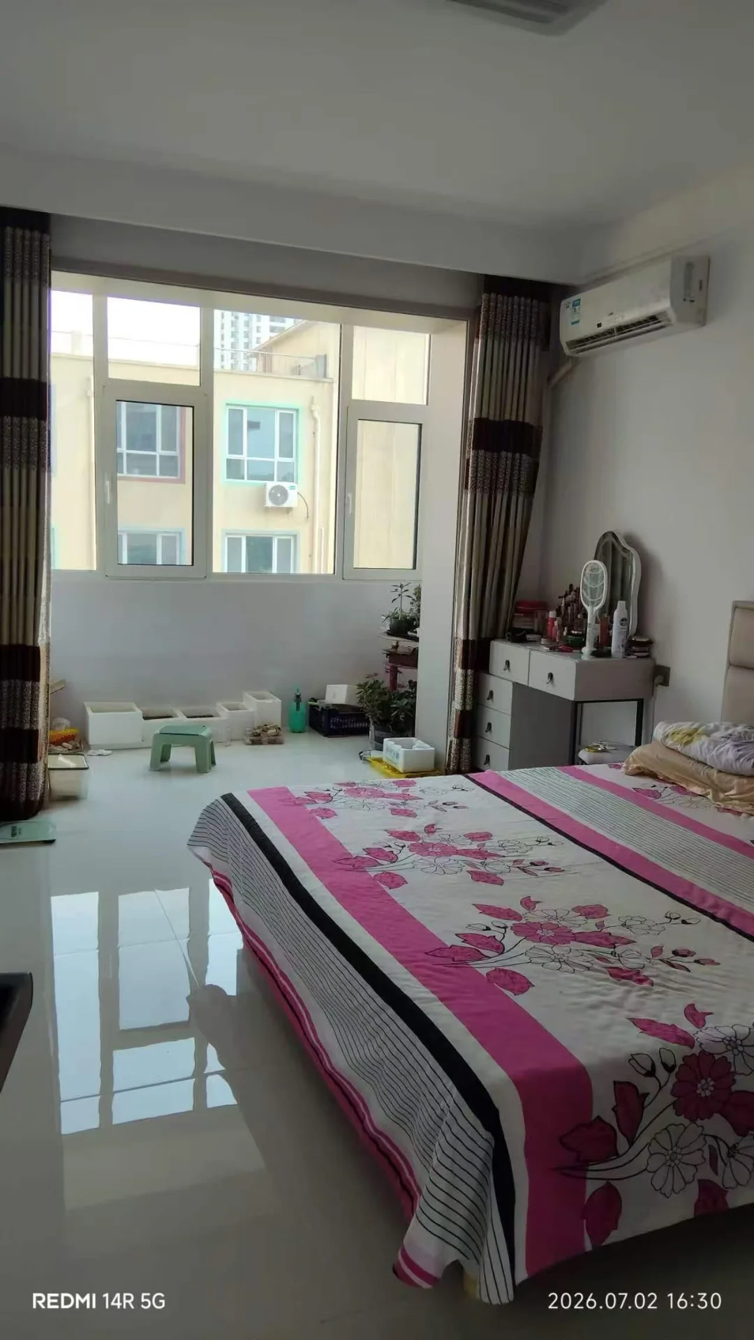 卧室空间，床铺铺设带有粉色花卉图案的床单，房间采光良好，整体呈现基础且整洁的居住环境。