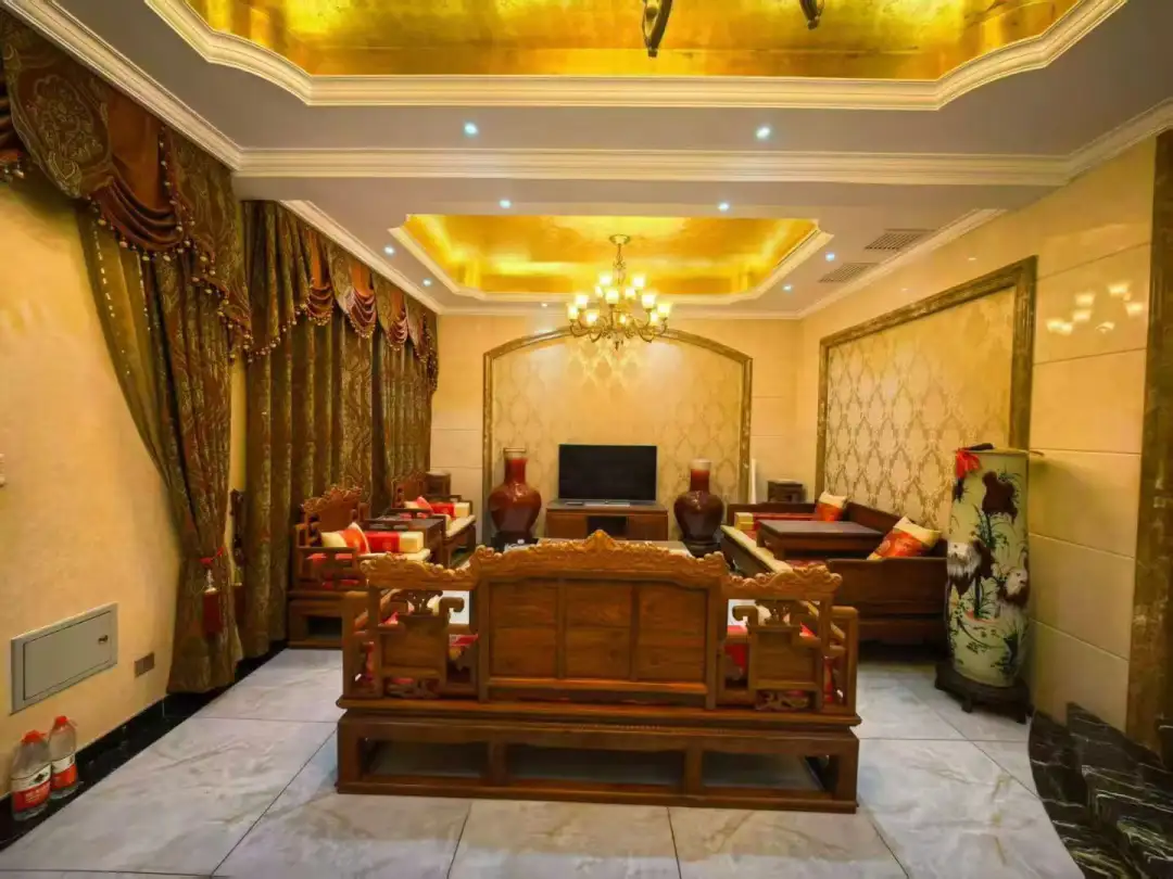 宽敞明亮的客厅，大窗户让自然光充足。木质地板和墙壁营造出温馨 inviting的氛围。吊灯悬挂在天花板上，增添优雅 touch。角落里一张复古风格的沙发搭配彩色抱枕，另一张沙发提供额外 seating options。墙上挂着电视，两侧放置两个 vases。整体布局和家具 arrangement创造一个放松或社交的 inviting and comfortable environment.关键字:关键词：客厅 大窗户 自然光 木质地板 墙壁 温馨氛围 吊灯 复古沙发 彩色抱枕 额外 seating options 电视机 花盆